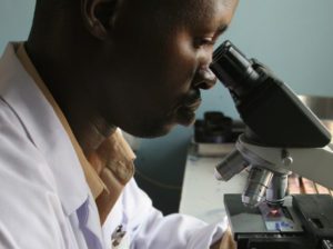 A health worker at a rural health clinic in Tanzania examines a specimen for presence of malaria. © 2007 Bonnie Gillespie, Courtesy of Photoshare